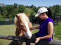 Portrait of a happy young girl giving to eat to a brown horse in ranch.