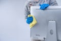 Young woman housekeeper in apron is doing cleaning silver computer screen with blue gloves, wet yellow rag, close up, copy space,