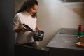 Young woman housewife takes out a stainless steel pan from the kitchen cabinet, standing at kitchen countertop Royalty Free Stock Photo