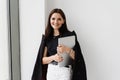 Young woman is hugging her laptop and smiling in cafe. Cheerful girl with laptop standing near big window in the white Royalty Free Stock Photo