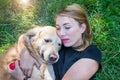 Woman is hugging her retriever while holding a red heart in her hand and lying on the grass in the park. Close-up Royalty Free Stock Photo