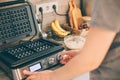 Young woman includes waffle iron, preparing Belgian waffles in the kitchen. Cooking process Royalty Free Stock Photo