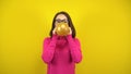 A young woman inflates a gold balloon with her mouth on a yellow background. Girl in a pink turtleneck and glasses. Royalty Free Stock Photo