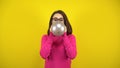 A young woman inflates a silver balloon with her mouth on a yellow background. Girl in a pink turtleneck and glasses. Royalty Free Stock Photo