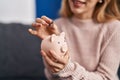 Young woman inserting coin on piggy bank at home Royalty Free Stock Photo