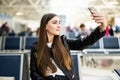 Young woman at international airport, making selfie with mobile phone and waiting for her flight. Female passenger at departure Royalty Free Stock Photo