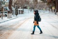 A young woman in a jacket and hat crosses a snow-covered empty street. Side view Royalty Free Stock Photo