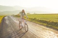 Young woman in jacket rides a bicycle over country road, afternoon sun shines at background Royalty Free Stock Photo