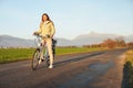 Young woman in jacket standing with a bicycle over country road, afternoon sun shines at mount Krivan peak - Slovak symbol - Royalty Free Stock Photo