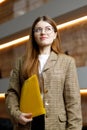 A young woman in a jacket with a yellow folder on the background of the office, purposefulness