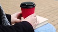 Young woman in jeans, coat and scarf, on a park bench. A woman is reading a book and drinking coffee or other hot drink outdoors Royalty Free Stock Photo