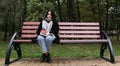 Young woman in jeans, coat and scarf, on a park bench. A woman is reading a book and drinking coffee or other hot drink outdoors Royalty Free Stock Photo