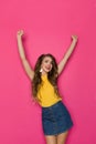 Young Woman In Jeans Mini Skirt And Yellow Top Is Standing With Arms Raised, Cheering And Shouting Royalty Free Stock Photo