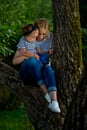 A young woman in jeans and a striped T-shirt and her little daughter are sitting on a tree Royalty Free Stock Photo