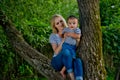 A young woman in jeans and a striped T-shirt and her little daughter are sitting on a tree Royalty Free Stock Photo