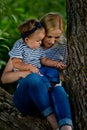 A young woman in jeans and a striped T-shirt and her little daughter are sitting on a tree Royalty Free Stock Photo