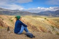 Young woman in jeans and sunglasses sitting against beautiful mountains and blue sky on sunny day. Freedom, tourism, adventure,