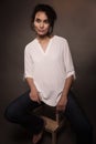 A young woman in jeans and a white shirt is sitting on a chair in a photo studio