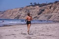 A young woman jogging barefoot on a Scripps beach