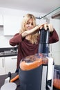 Young woman juicing carrots in kitchen