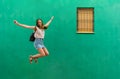 Young woman is jumping while she is listening music on green background Royalty Free Stock Photo