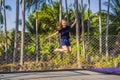 Young woman jumping on an outdoor trampoline, against the backdrop of palm trees