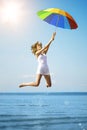 Young woman jumping with rainbow umbrella on the beach. Scene of Royalty Free Stock Photo