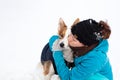 Young woman kissing her cute mixed breed dog, snowy winter background