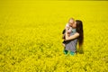 Young woman kissing little baby in bright yellow flower field in sunny summer day, family love and sincerity