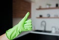 Young woman in kitchen during quarantine. Female hand in green glove hold big thumb up. Kitchen interior with blurred Royalty Free Stock Photo