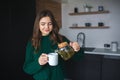 Young woman in kitchen during quarantine. Girl pouring some tea from teapot into white cup. Beautiful woman in green Royalty Free Stock Photo