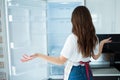 Young woman on kitchen during quarantine. Look at empty fridge shelves with no food on it. Hungry and can`t cook. Back