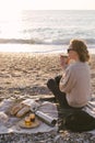 Woman having picnic at beach with tea in thermos.