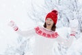 Young woman in knitted sweater playing snow ball fight in winter. Girl in family snow balls game. Female in knit handmade hat and