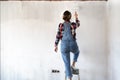 Young woman on a ladder painting new apartment walls in color white with paint roller. Renovating house Royalty Free Stock Photo