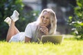 Young woman with laptop lies on the grass in a summer park. Laughing blonde with long hair in a white tank top and shorts. Sunny Royalty Free Stock Photo