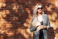 Young woman with laptop stands against a brick wall. Smiling blonde in sunglasses in bright sunlight. Remote work and distance