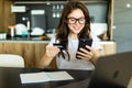 Happy young woman with laptop using credit card and phone in kitchen at home Royalty Free Stock Photo