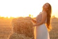 Young woman lean on haystack walking in summer evening, beautiful romantic girl outdoors in field at sunset Royalty Free Stock Photo