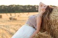 Young woman lean on haystack walking in summer evening, beautiful romantic girl outdoors in field at sunset Royalty Free Stock Photo