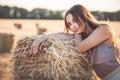 Young woman lean on haystack walking in summer evening, beautiful romantic girl outdoors in field at sunset Royalty Free Stock Photo