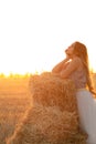 Young woman lean on haystack walking in summer evening, beautiful romantic girl outdoors in field at sunset Royalty Free Stock Photo