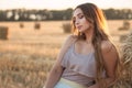 Young woman lean on haystack walking in summer evening, beautiful romantic girl outdoors in field at sunset Royalty Free Stock Photo