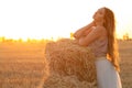 Young woman lean on haystack walking in summer evening, beautiful romantic girl outdoors in field at sunset Royalty Free Stock Photo