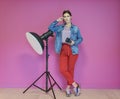 Young woman leaning against studio flashlight and holding camera over a pink background Royalty Free Stock Photo