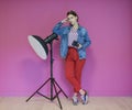 Young woman leaning against studio flashlight and holding camera over a pink background Royalty Free Stock Photo