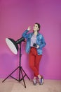 Young woman leaning against studio flashlight and holding camera over a pink background Royalty Free Stock Photo