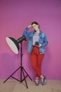 Young woman leaning against studio flashlight and holding camera over a pink background Royalty Free Stock Photo