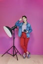 Young woman leaning against studio flashlight and holding camera over a pink background Royalty Free Stock Photo