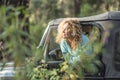 Young woman leaning outside car window and looking at forest. Beautiful woman enjoying holiday trip in forest. Happy woman Royalty Free Stock Photo